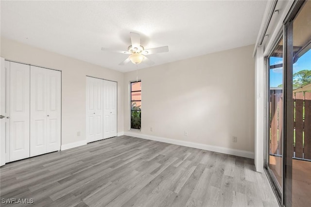 unfurnished bedroom featuring access to outside, multiple windows, two closets, and light wood-style flooring