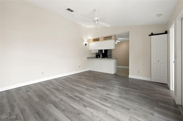 unfurnished living room with lofted ceiling, a barn door, wood finished floors, visible vents, and a ceiling fan