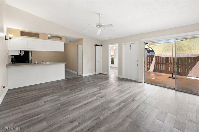 unfurnished living room with a barn door, ceiling fan, vaulted ceiling, wood finished floors, and baseboards