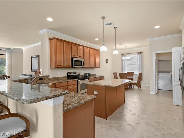 kitchen featuring pendant lighting, appliances with stainless steel finishes, a kitchen breakfast bar, washer / clothes dryer, and kitchen peninsula