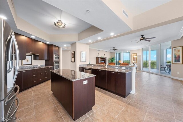 kitchen featuring dark brown cabinetry, stainless steel appliances, light stone countertops, and a kitchen island with sink