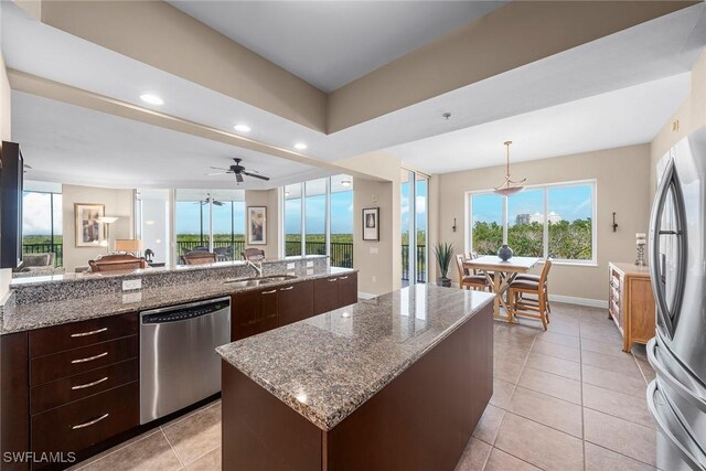 kitchen featuring stainless steel appliances, light stone countertops, a kitchen island, and a wealth of natural light