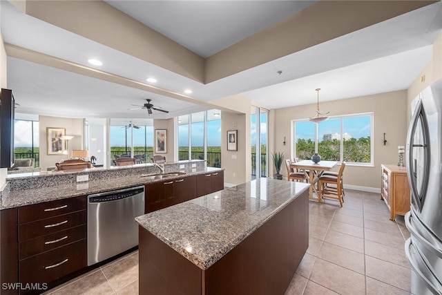 kitchen with a sink, stainless steel appliances, light tile patterned flooring, light stone countertops, and dark brown cabinets