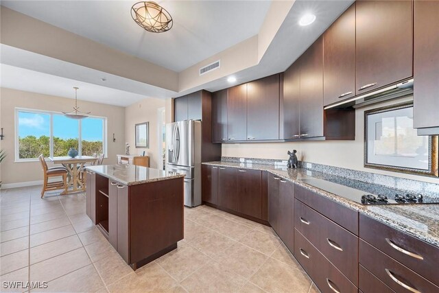 kitchen with decorative light fixtures, dark brown cabinets, a kitchen island, black electric stovetop, and light stone countertops