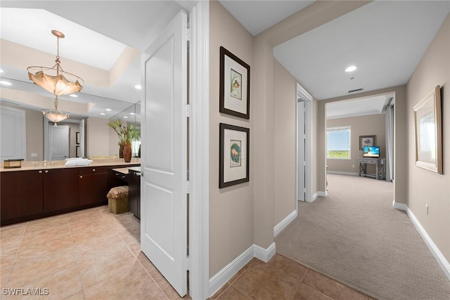 corridor featuring light tile patterned floors, baseboards, and light carpet