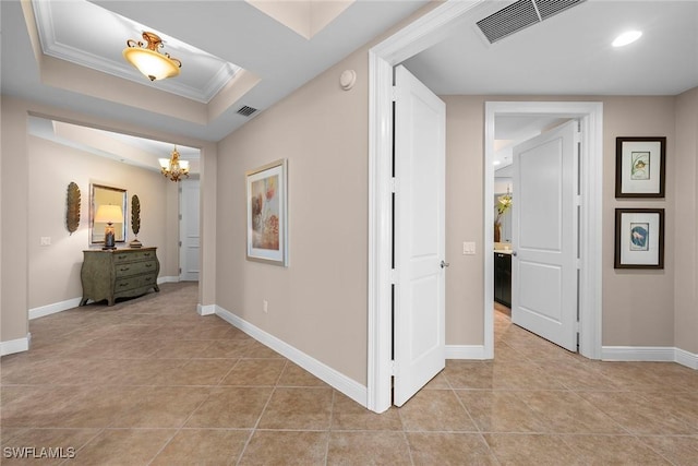 hallway with an inviting chandelier, light tile patterned floors, ornamental molding, and a raised ceiling