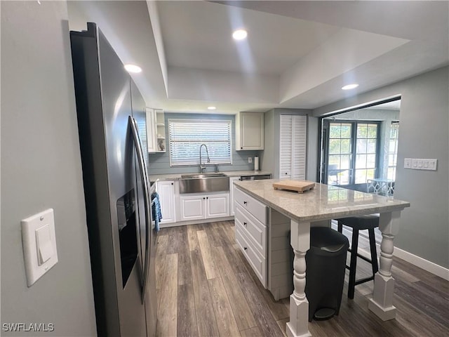 kitchen with sink, a breakfast bar, a tray ceiling, a kitchen island, and stainless steel fridge with ice dispenser