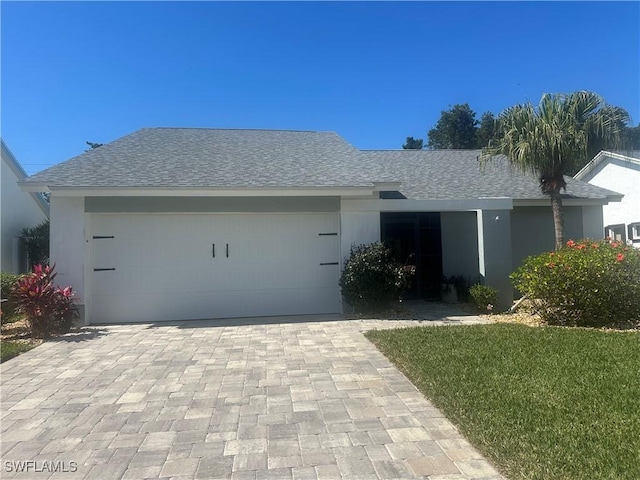 ranch-style house with decorative driveway, roof with shingles, and an attached garage