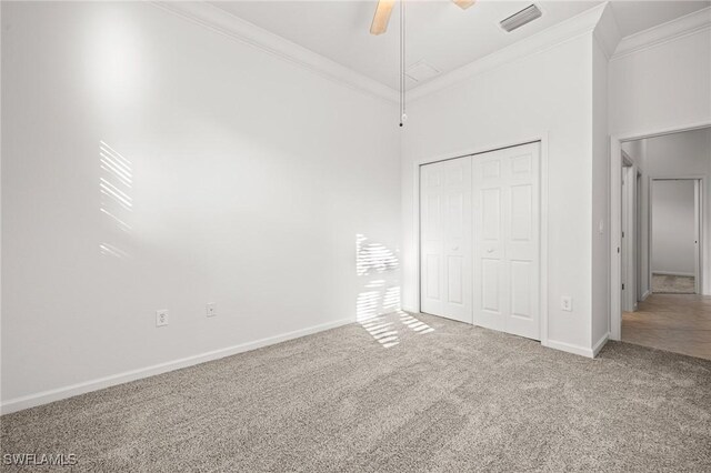 unfurnished bedroom with a closet, ornamental molding, carpet, and a high ceiling