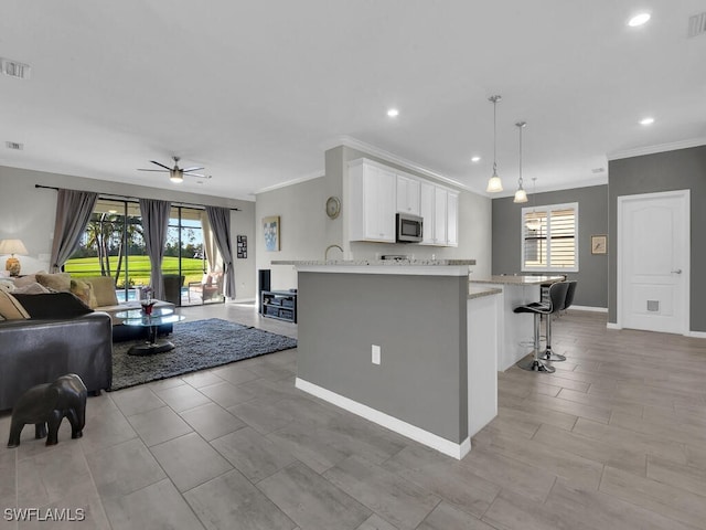 kitchen featuring decorative light fixtures, a breakfast bar area, white cabinets, kitchen peninsula, and plenty of natural light