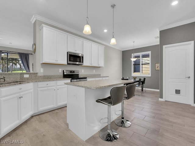 kitchen with hanging light fixtures, ornamental molding, appliances with stainless steel finishes, a kitchen island, and white cabinets