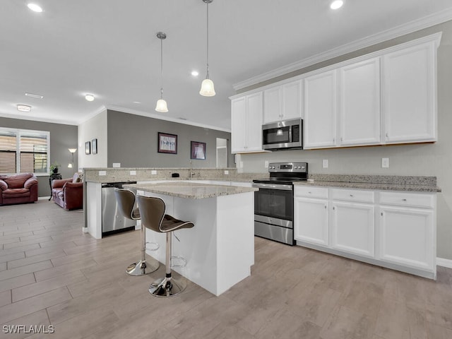 kitchen with appliances with stainless steel finishes, white cabinetry, hanging light fixtures, a kitchen breakfast bar, and light stone counters