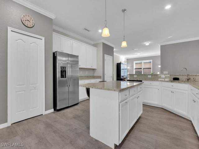 kitchen with sink, stainless steel fridge, light stone counters, white cabinets, and a kitchen island