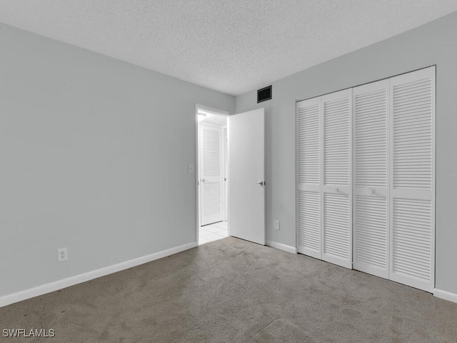 unfurnished bedroom with light colored carpet, a textured ceiling, and a closet