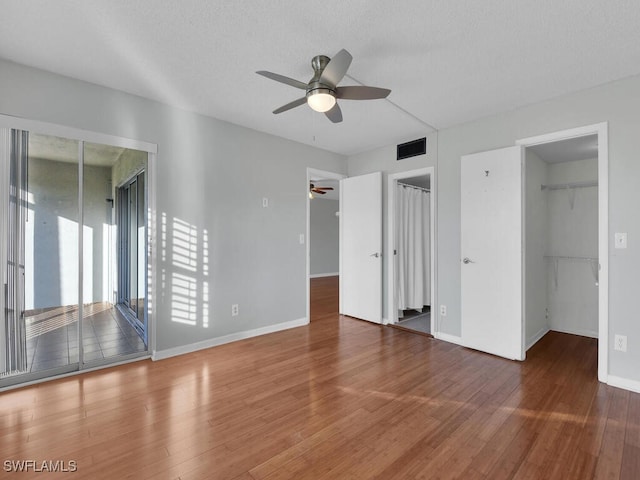 unfurnished bedroom featuring hardwood / wood-style flooring, a spacious closet, access to exterior, ceiling fan, and a textured ceiling