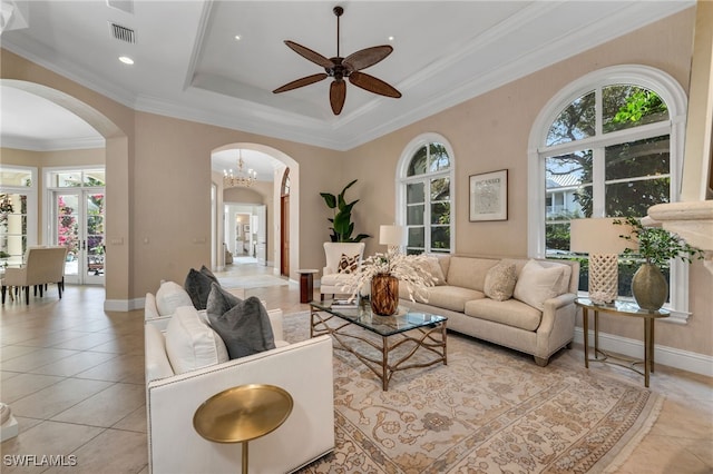 tiled living room with ceiling fan with notable chandelier, ornamental molding, a raised ceiling, and a healthy amount of sunlight