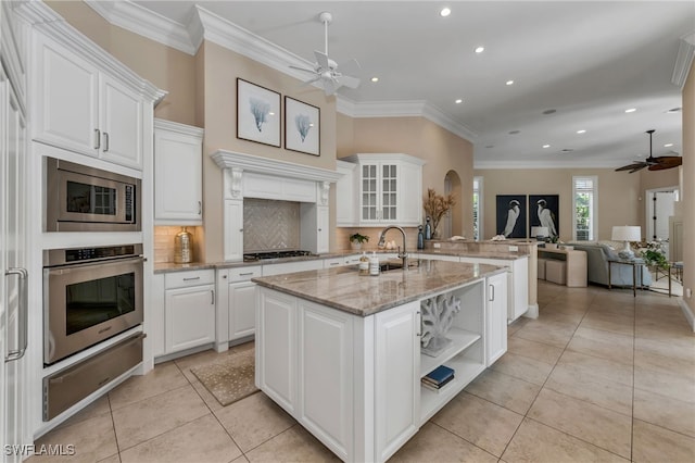 kitchen featuring ceiling fan, appliances with stainless steel finishes, light stone counters, an island with sink, and white cabinets