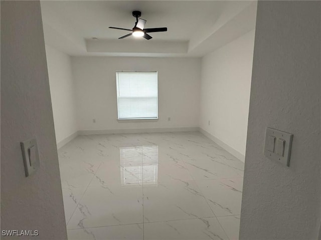 spare room with ceiling fan and a raised ceiling