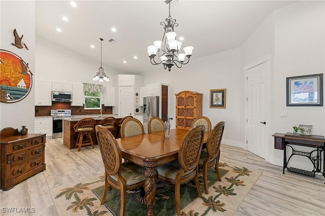 dining room with an inviting chandelier, high vaulted ceiling, and light hardwood / wood-style floors