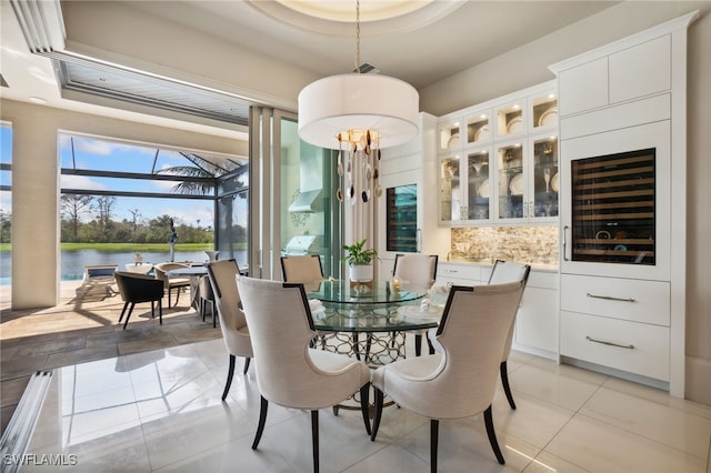 dining area with light tile patterned flooring, a water view, and a tray ceiling