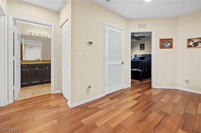 hallway with light wood-type flooring, a sink, visible vents, and baseboards