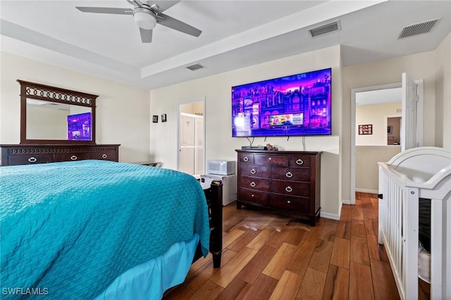 bedroom with a raised ceiling, wood finished floors, and visible vents