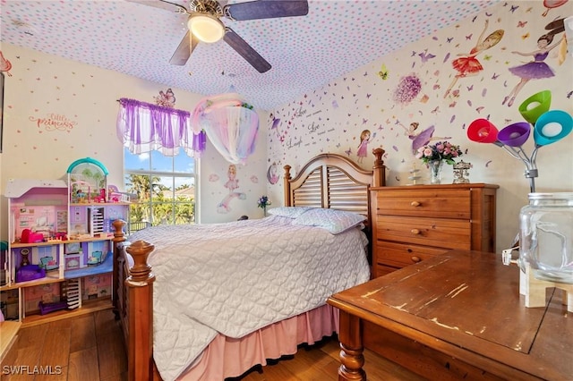 bedroom with wallpapered walls, a ceiling fan, and wood finished floors