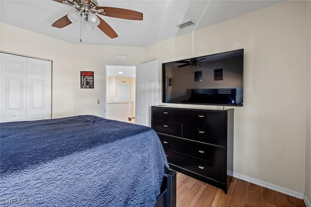 bedroom with ceiling fan, wood finish floors, visible vents, baseboards, and a closet