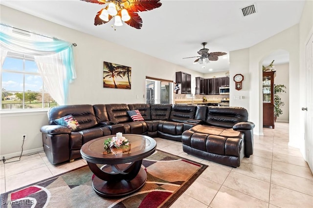 living area featuring arched walkways, light tile patterned floors, visible vents, ceiling fan, and baseboards