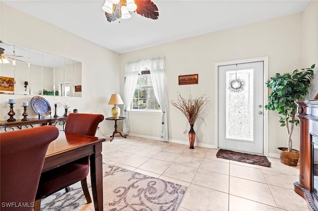 dining space featuring light tile patterned floors, a glass covered fireplace, a ceiling fan, and baseboards