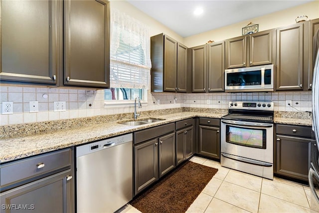 kitchen with tasteful backsplash, light stone countertops, stainless steel appliances, a sink, and light tile patterned flooring