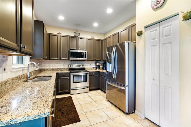 kitchen featuring light tile patterned floors, light stone counters, stainless steel appliances, a sink, and decorative backsplash