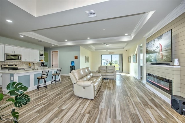 living room with a raised ceiling, crown molding, and sink