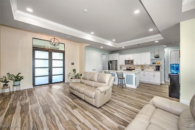 living room with a raised ceiling, crown molding, light wood-type flooring, and french doors