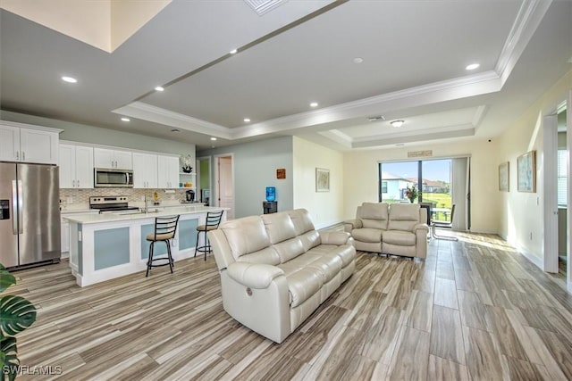 living room featuring light hardwood / wood-style flooring, ornamental molding, and a raised ceiling