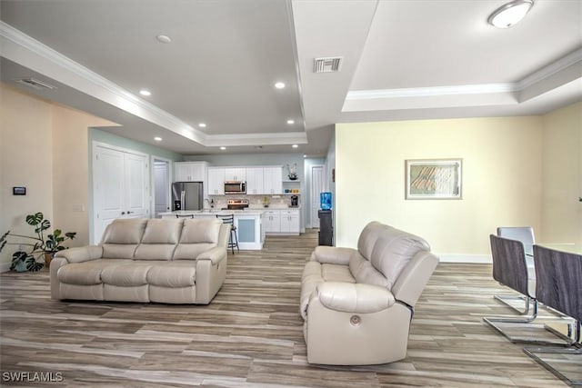 living room featuring ornamental molding, a tray ceiling, and light hardwood / wood-style floors