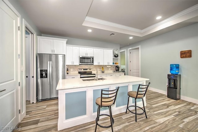 kitchen featuring stainless steel appliances, a center island with sink, and a tray ceiling