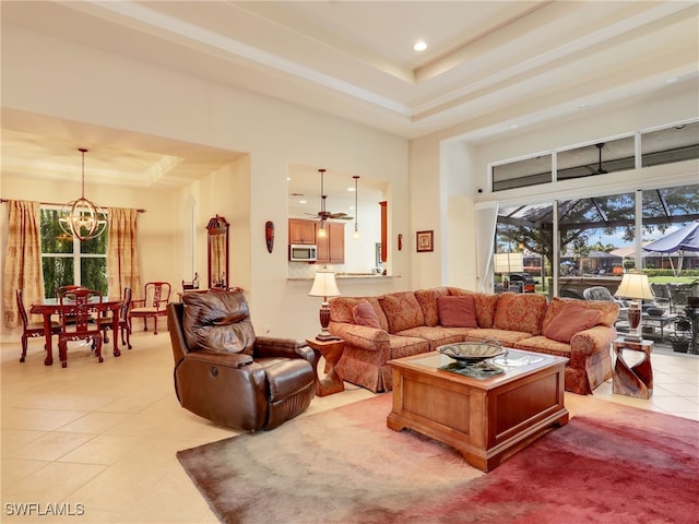 tiled living room with a raised ceiling, ceiling fan with notable chandelier, and a high ceiling