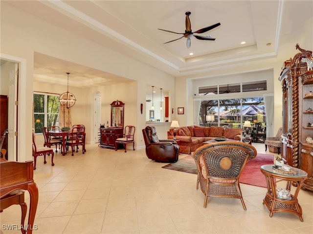 living room featuring a high ceiling, ceiling fan with notable chandelier, light tile patterned floors, and a tray ceiling