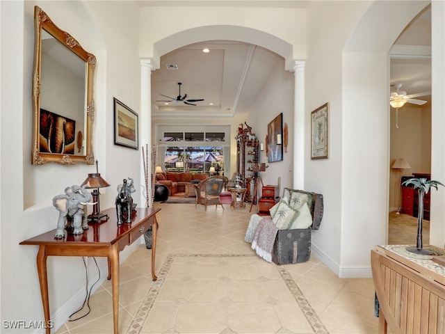 hall featuring a tray ceiling, decorative columns, and light tile patterned floors