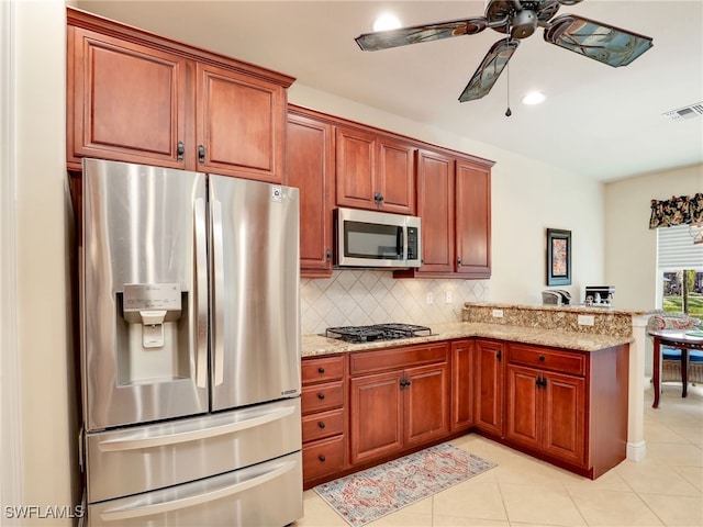 kitchen with appliances with stainless steel finishes, kitchen peninsula, ceiling fan, light stone countertops, and decorative backsplash