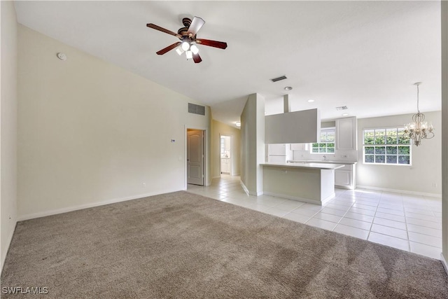 unfurnished living room featuring ceiling fan with notable chandelier, light colored carpet, and vaulted ceiling