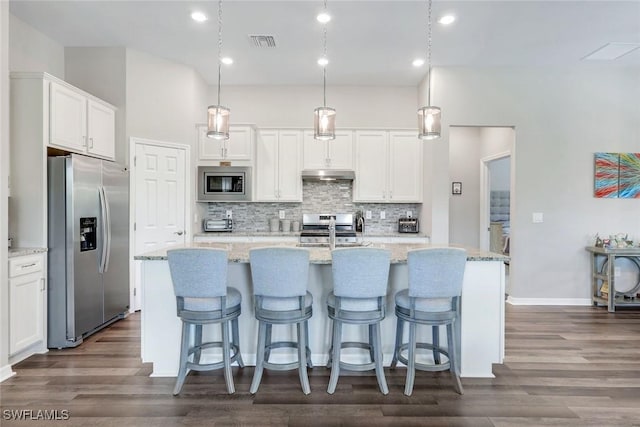 9368 Night Heron Ln, Naples, FL 34120 - kitchen featuring stainless steel appliances, under cabinet range hood, decorative backsplash, dark wood-style floors, and white cabinets