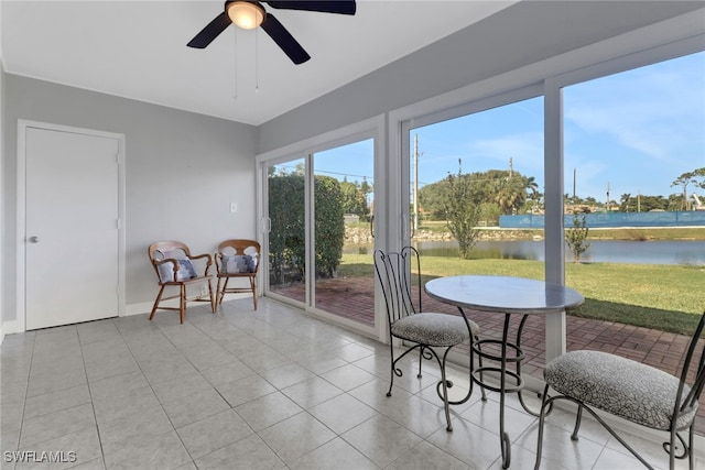 sunroom with ceiling fan and a water view