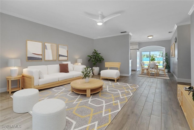 living room featuring arched walkways, baseboards, ornamental molding, and wood finished floors