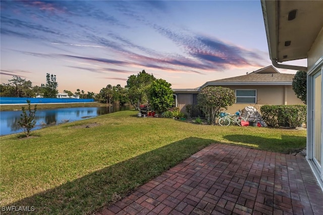 yard at dusk with a water view and a patio