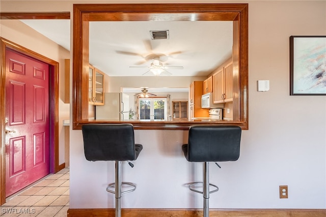 kitchen featuring white appliances, a breakfast bar area, kitchen peninsula, and light tile patterned flooring