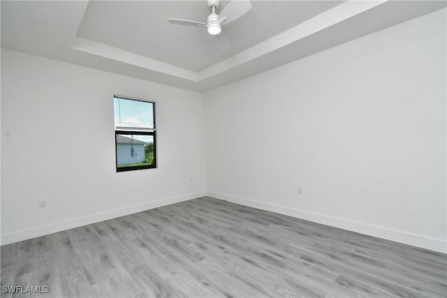 unfurnished room with ceiling fan, a tray ceiling, and light hardwood / wood-style floors