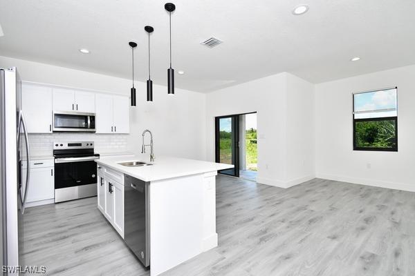 kitchen with white cabinetry, sink, hanging light fixtures, a kitchen island with sink, and stainless steel appliances