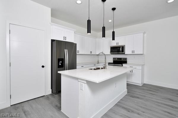 kitchen featuring sink, white cabinetry, hanging light fixtures, stainless steel appliances, and a kitchen island with sink